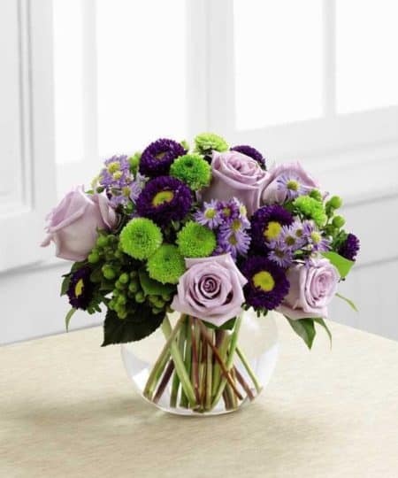 A floral design of roses and asters creates the perfect bouquet for any of life's special moments. Deep Purple lavender roses, lavender Monte Casino asters, purple matsumoto asters, green hypericum berries, green button mums, and lush greens create a stunning bouquet perfectly arranged in a clear glass bubble bowl vase to create a wonderful thank you, Happy Birthday or Congratulations gift.